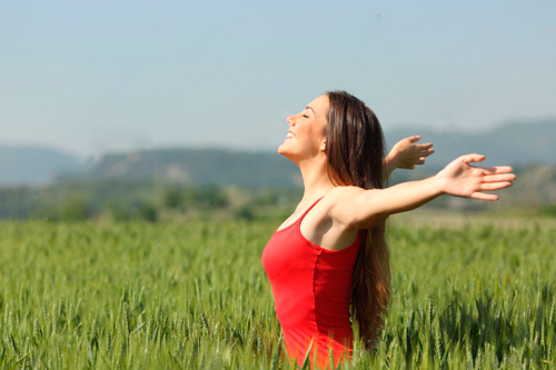 Chica en un campo con camiseta roja y respirando en libertad.